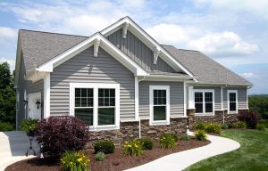 White double-hung windows and trim on gray suburban home with mix of vinyl siding and stone veneer