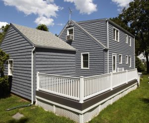 Two-story suburban home with gray siding and white fence around backyard deck