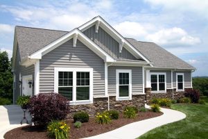 Gray vinyl siding and stone veneer on suburban home with white windows and trim